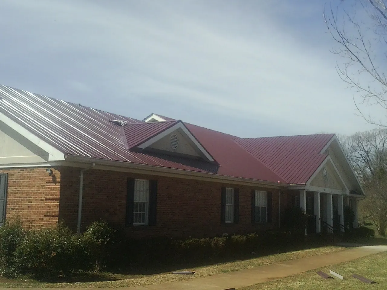 Red metal roof with gabled entries on a long brick building, from a Hail Damage Roof Repair job in Fountain